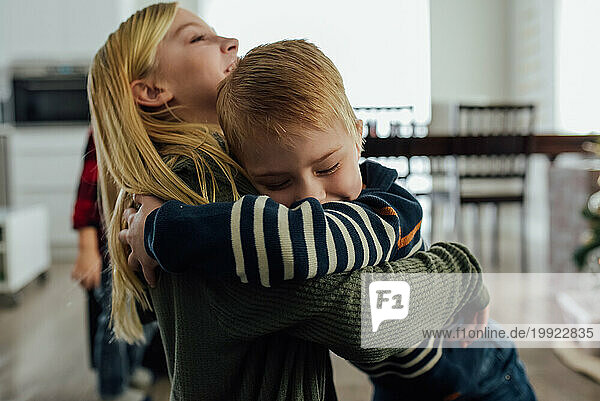 Close up of little boy giving sister a huge hug in living room a