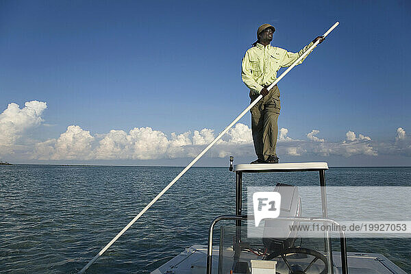 Bonefishing guide poles his boat in shallow waters near Andros Island Bonefish Club
