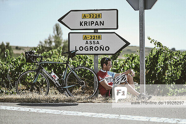 Cyclist resting on roadside near directional signs  Pamplona  Navarre  Spain