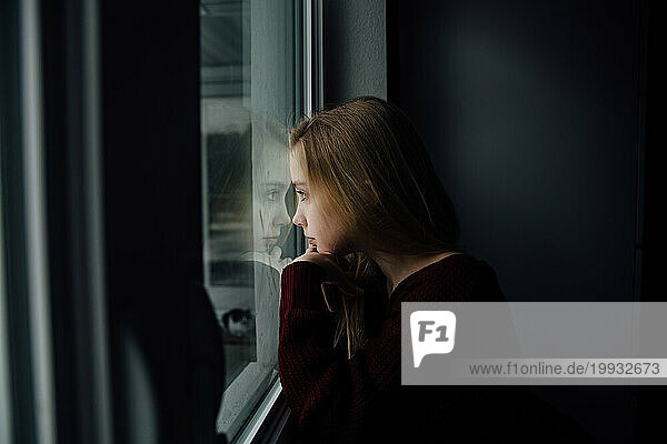 Serious preteen girl touches forehead to window with reflection