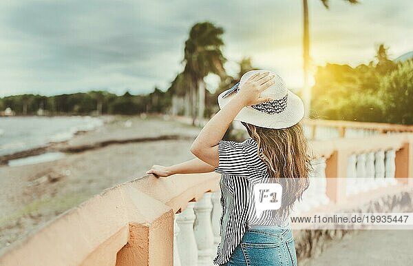Rückansicht eines schönen Mädchens auf einem Pier mit Hut in der Hand. Tourist Frau in der Nähe eines Hafens hält ihren Hut
