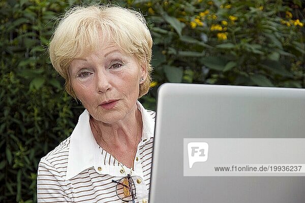 Seniorin mit Laptop im Garten