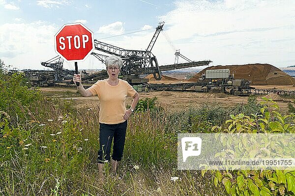 Frau steht am Rande eines Tagebaues und protestiert gegen die Umweltzerstörung