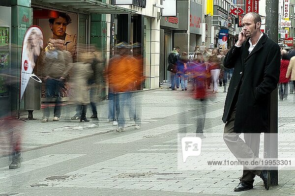 Junger Mann steht in einer Einkaufsstrasse und telefoniert mit seinem Handy