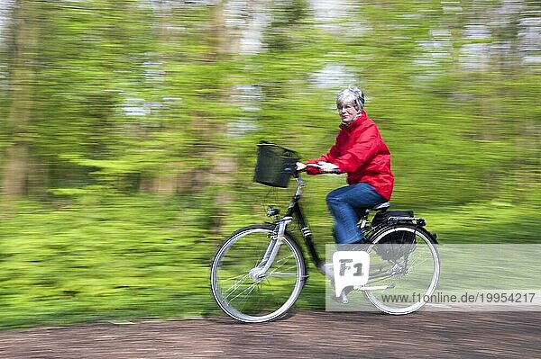 Seniorin fährt mit einem Fahrrad schnell durch den Wald