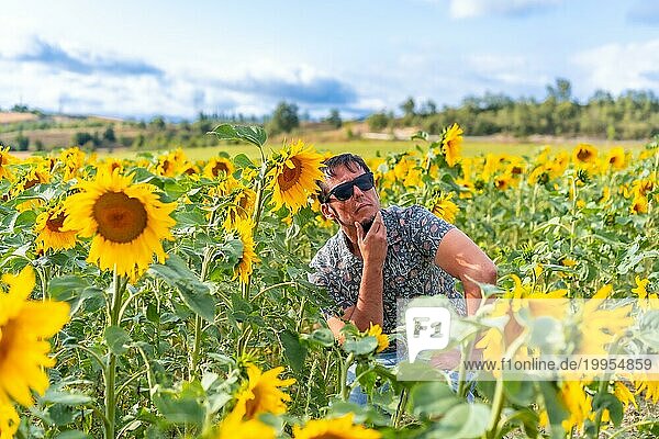 Nachdenklicher Mann mit Sonnenbrille zwischen Sonnenblumen genießt den Sommer