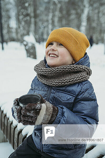 Smiling boy with tea cup sitting in winter park