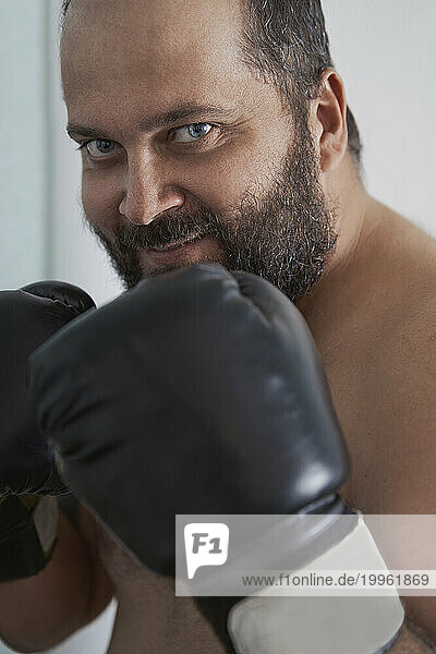 Smiling man wearing boxing gloves at home