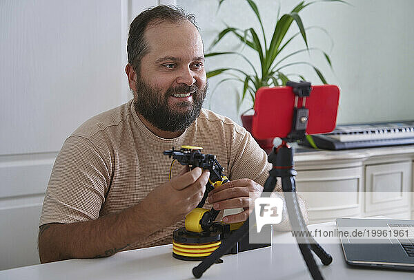 Smiling engineer giving presentation and vlogging over robotic arm on smart phone at home