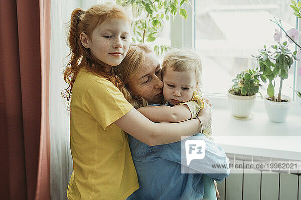 Mother and daughters hugging each other at home