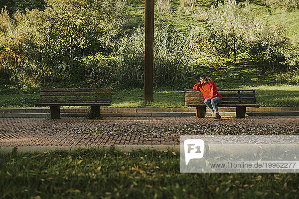Thoughtful woman sitting on bench in autumn park