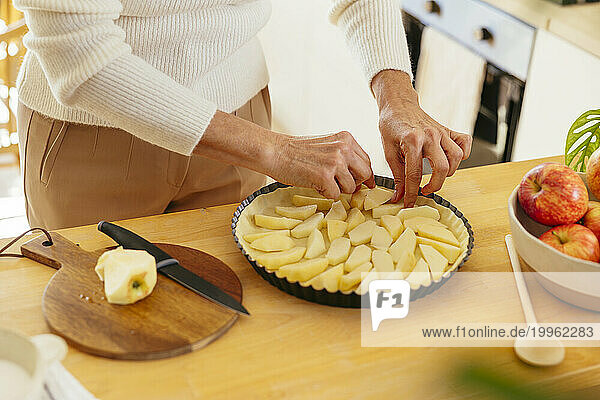 Mature woman arranging apple pieces on pie at home