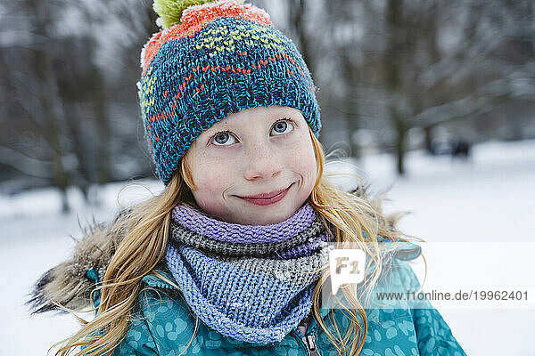 Smiling blond girl wearing scarf and knit hat in winter