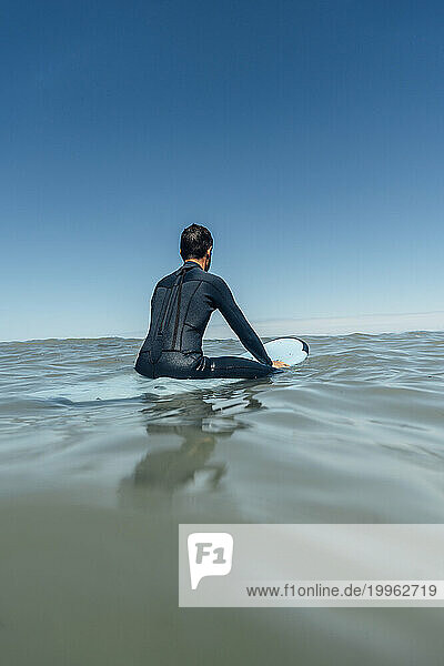 Surfer with surfboard over sea under clear blue sky on sunny day