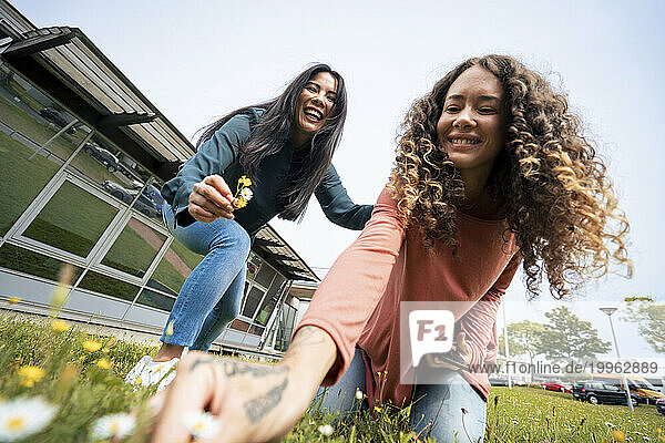 Happy multiracial friends plucking flowers in front of sky