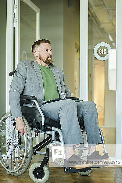 Businessman sitting in wheelchair near glass door