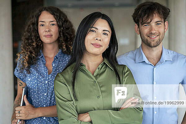 Confident businesswoman with arms crossed standing by colleagues in lobby
