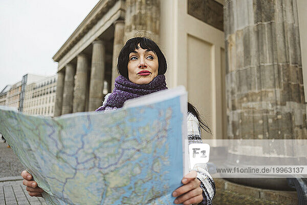 Contemplative woman with map standing on footpath