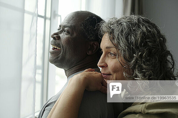 Mature couple looking through window and spending leisure time at home
