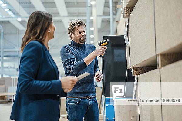 Smiling businessman scanning bar code on wooden plank by colleague in industry