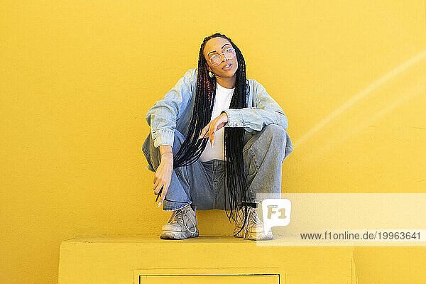 Woman with braided hair crouching in front of yellow wall