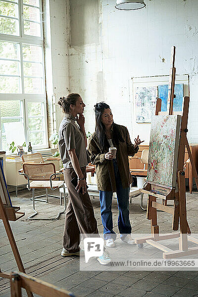Confident women discussing over painting on easel in art studio