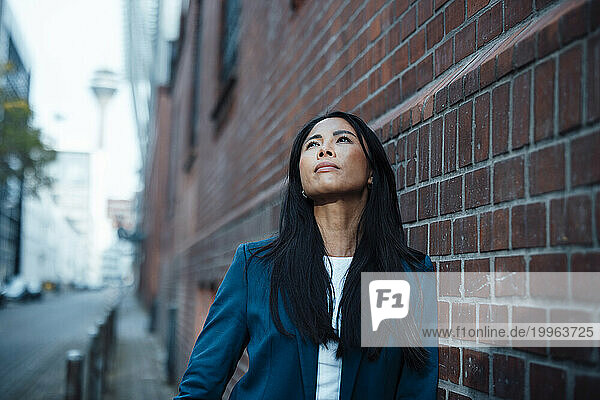 Thoughtful businesswoman standing near brick wall
