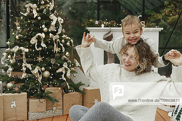 Happy mother and son having fun near Christmas tree at home