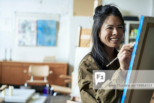 Smiling painter painting on canvas in art studio