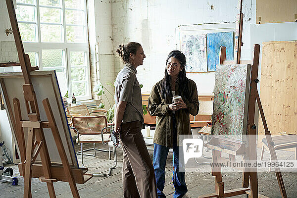 Smiling women discussing over painting on easel in art studio