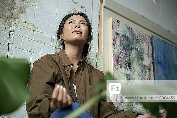 Smiling painter sitting cross-legged by paintings at art studio