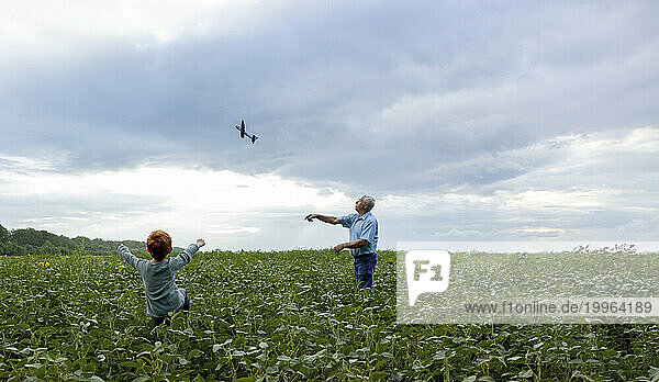 Grandfather and grandson flying toy airplane in field