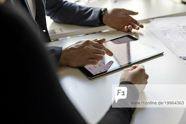 Hand of businessman using tablet computer by colleague at desk in workplace
