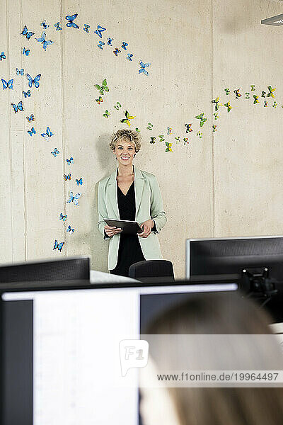 Businesswoman with tablet computer standing in front of wall at office