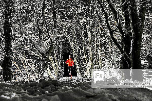 Man running on snow under trees in winter forest at night