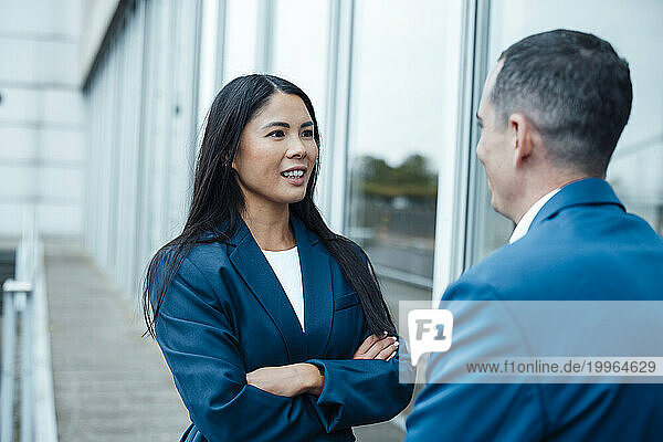 Smiling businesswoman and businessman discussing near building
