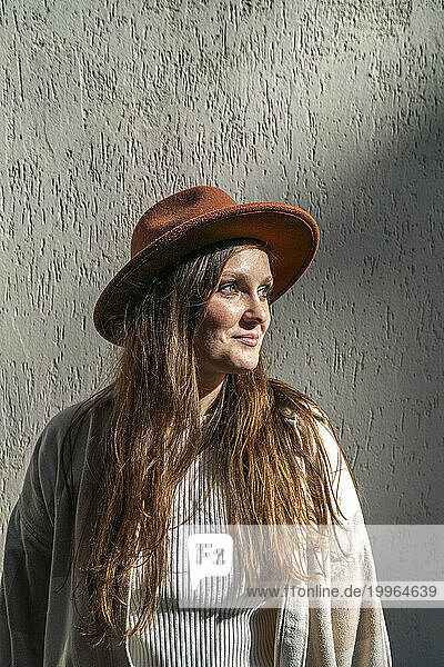 Smiling young woman wearing hat and standing in front of wall