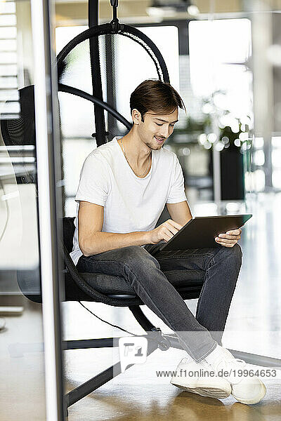 Young businessman using tablet PC sitting on chair in office
