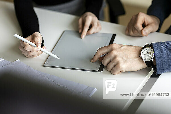 Hands of colleagues with tablet PC on desk in office