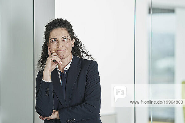 Thoughtful businesswoman leaning on glass door in office