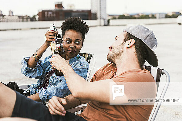 Smiling couple toasting beer bottles on terrace