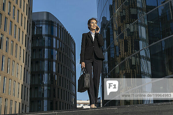 Smiling businesswoman talking on smart phone and walking in city