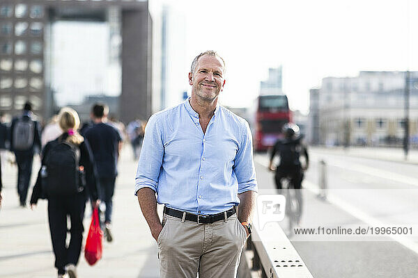 Smiling businessman standing with hands in pockets on footpath at London  UK