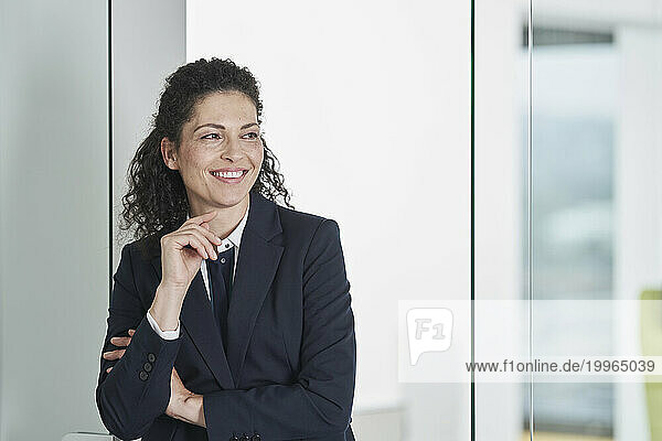 Happy mature businesswoman leaning on glass door in office