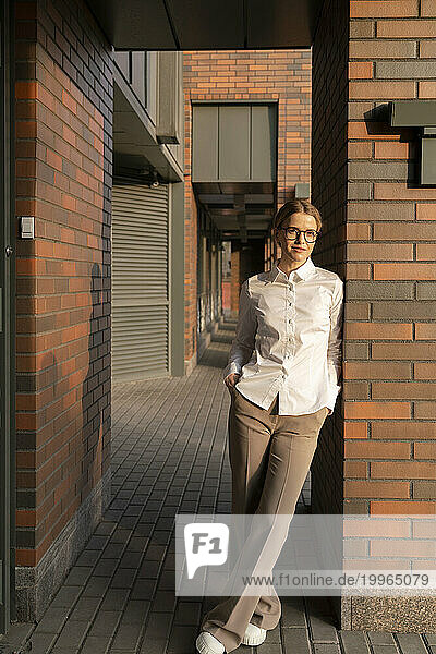 Businesswoman with legs crossed at ankle leaning on brick wall