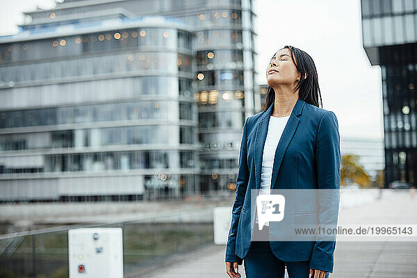 Businesswoman standing with eyes closed near buildings