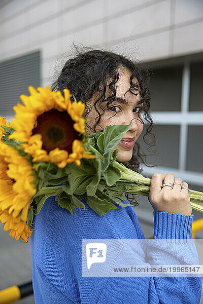 Smiling woman holding bunch of sunflowers near building