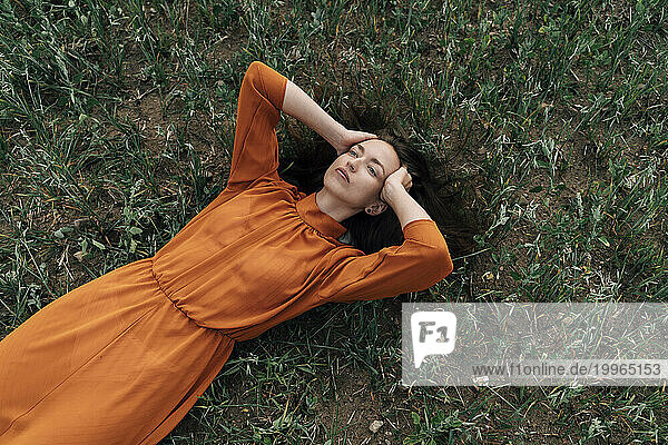 Thoughtful woman with hand in hair lying in field