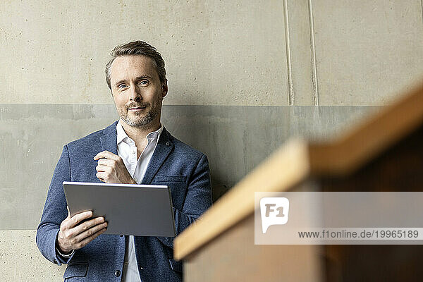 Confident businessman with tablet PC in front of wall