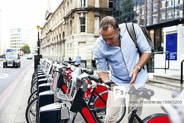 Businessman renting electric bicycle with smart phone at street